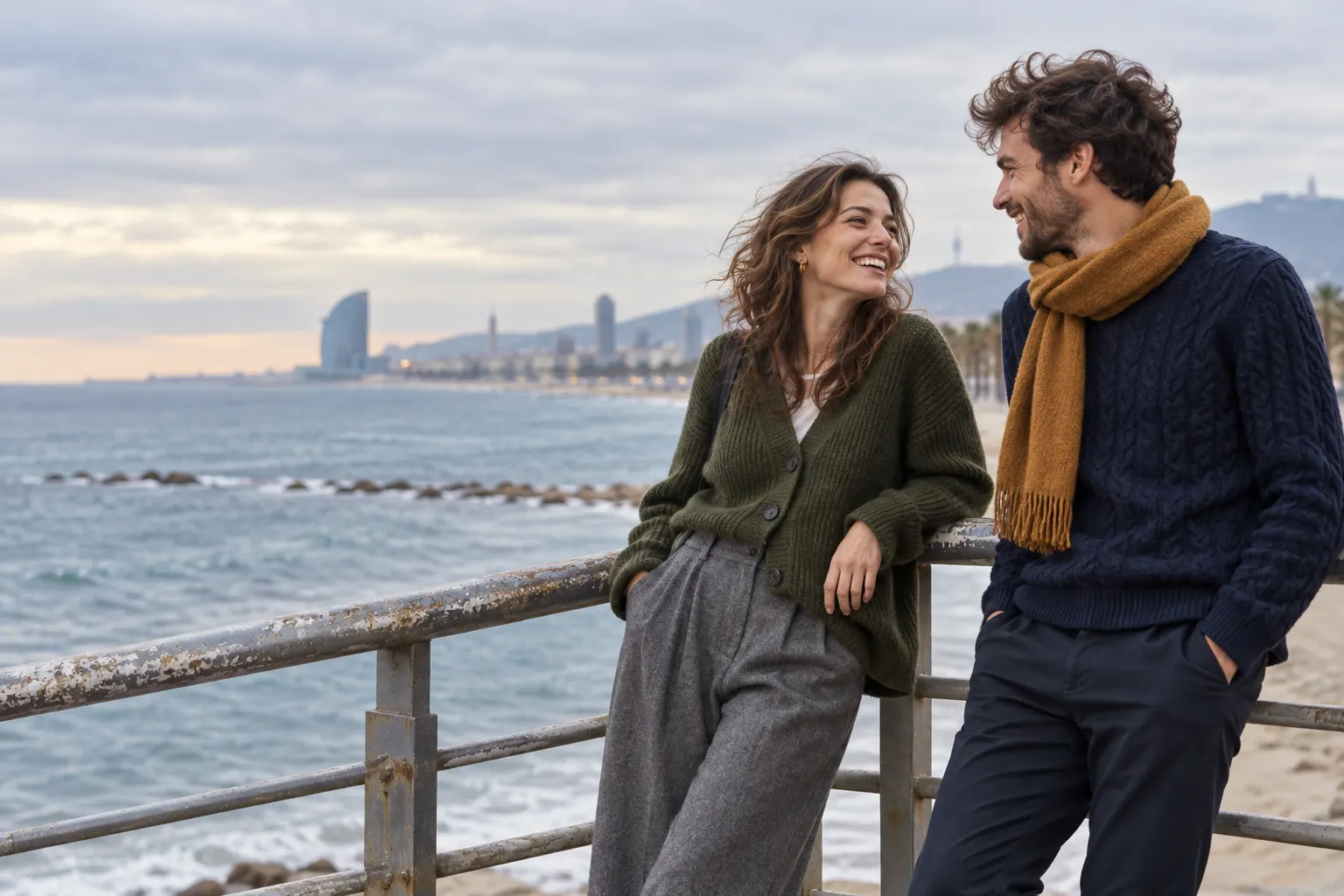 Pareja con cárdigan verde oliva y jersey de ochos marino apoyada en la barandilla del paseo marítimo